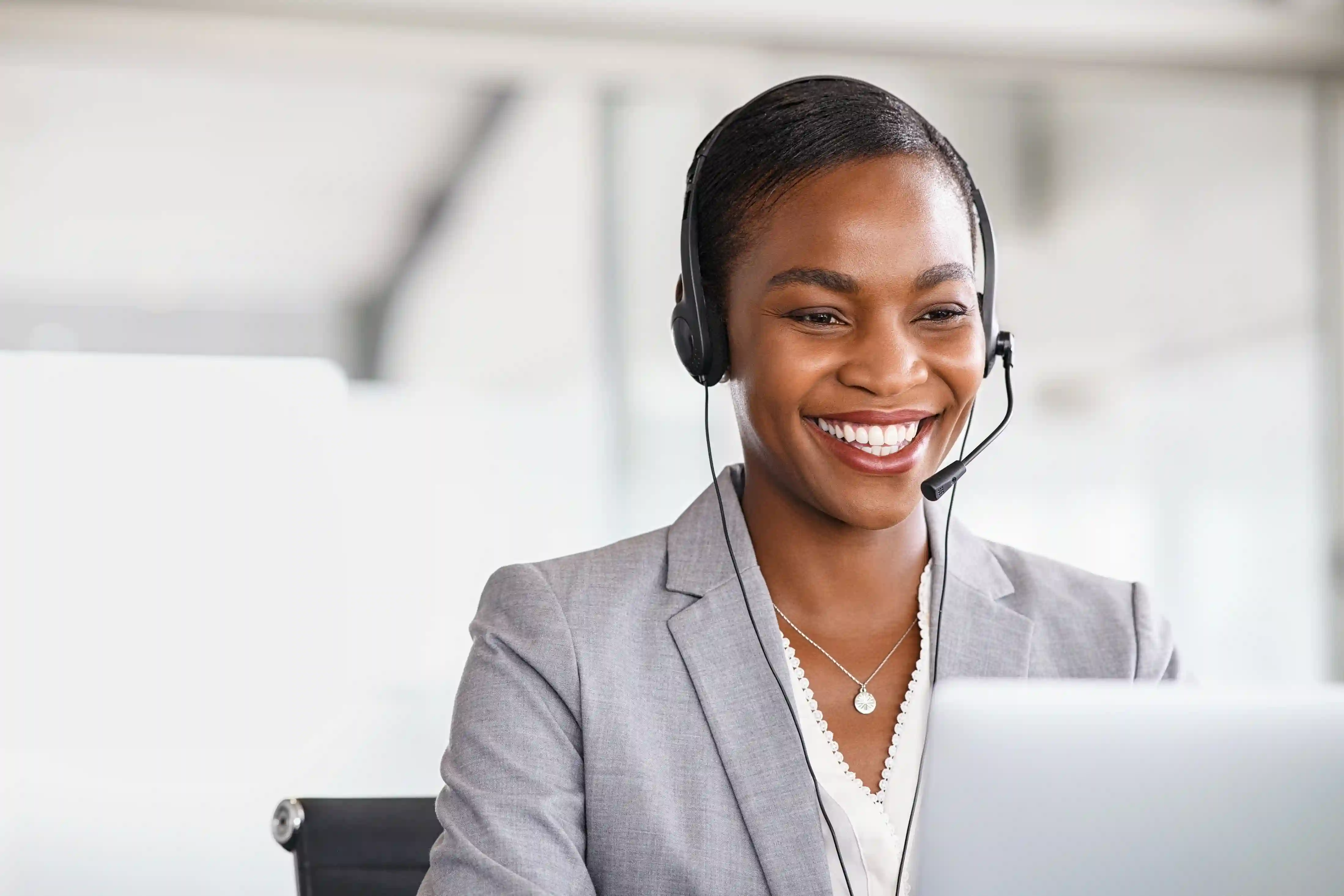 A smiling customer service representative wearing a headset working on a laptop computer