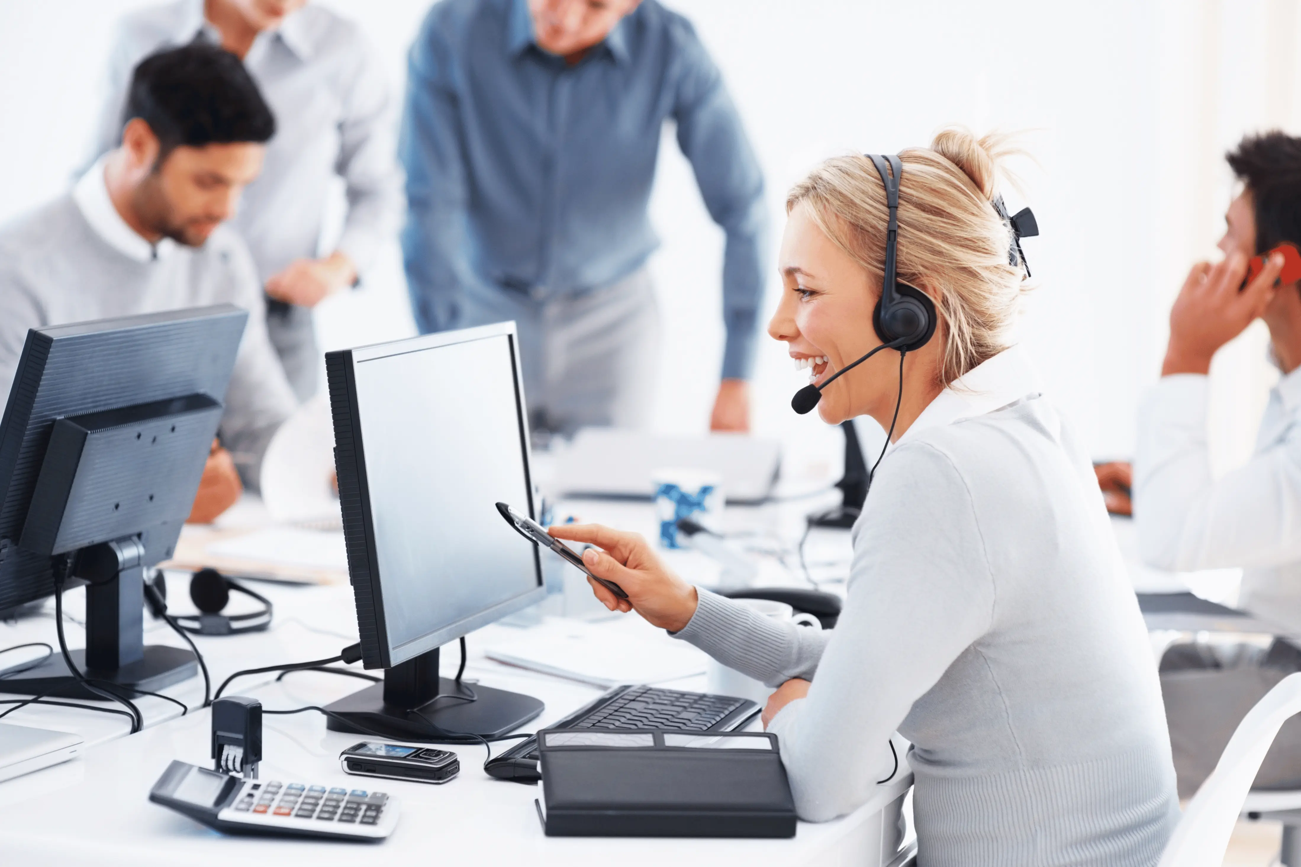 A smiling customer service representative wearing a headset working on a laptop computer