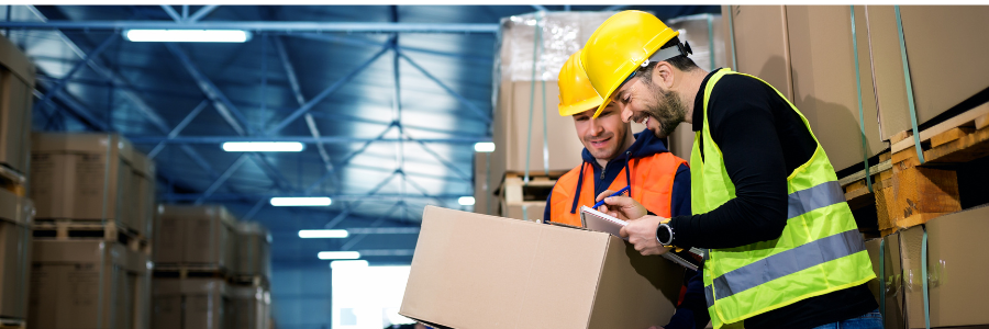 Two warehouse workers smiling and looking at boxed products.