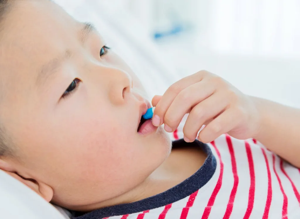 Small child laying down placing a blue capsule into his mouth.