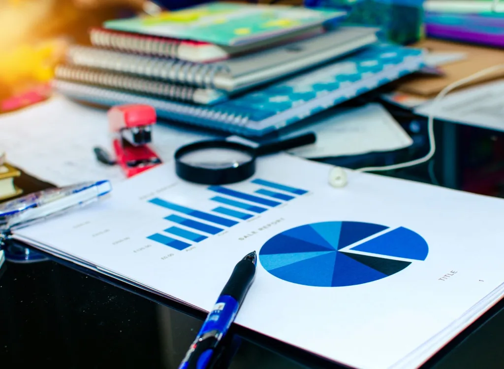 Close up shot of notebooks and paper with printed metrics along with a magnifying glass, stapler, and pen.