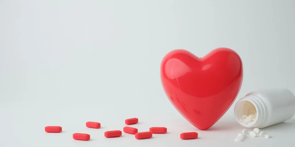 Photo of plastic heart next to red pills and empty pill bottle.