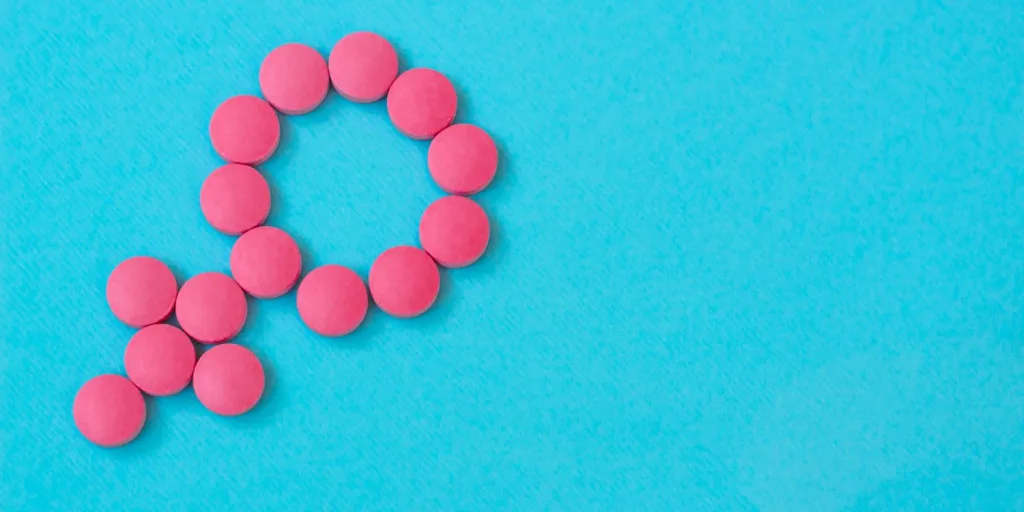 Pink round tablets arranged in the female gender symbol against a blue background.