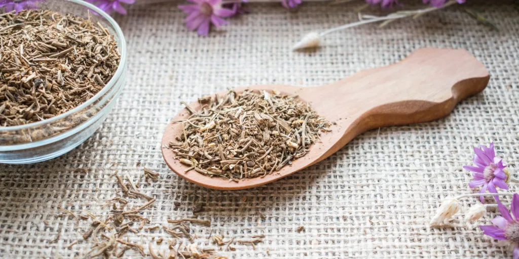 Shredded Agnus Castus plant in bowl and wooden spoon surrounded by purple Agnus Castus flowers.