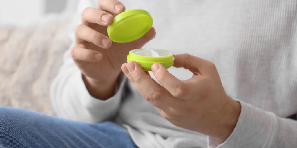 A closeup shot of a person holding a green, circle-shaped pill organizer.