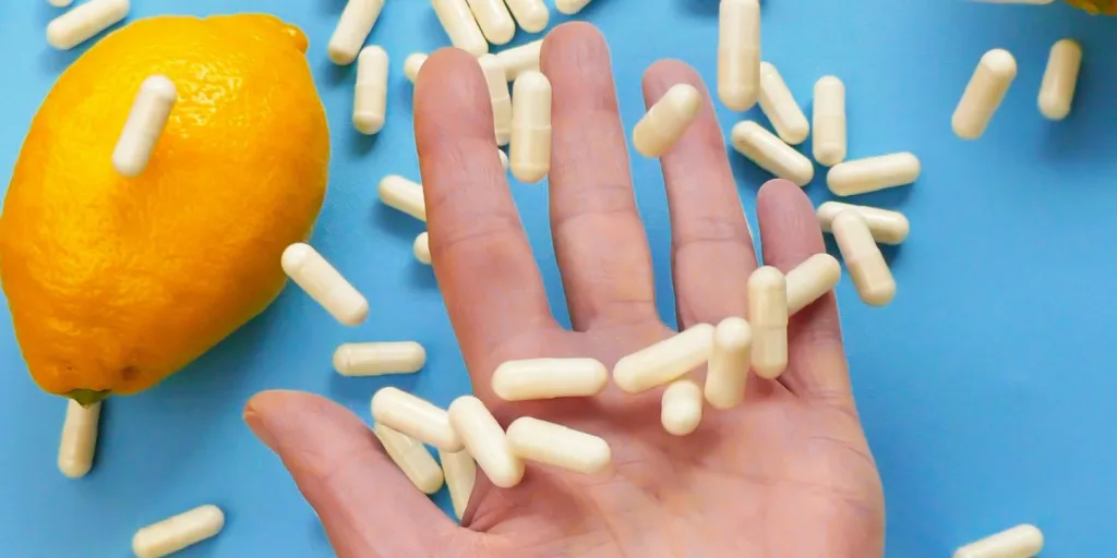 A hand catching filled capsules next o an orange against a blue background.