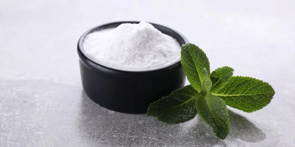A small bowl of fructose aside a small cluster of mint leaves.