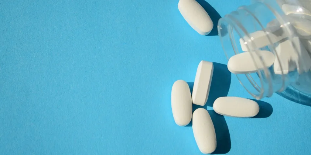 White tablets spilling from a clear bottle against a light blue background.