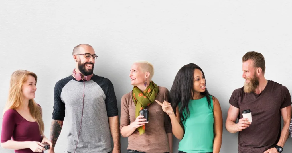 A group of people ranging in different ages standing against a white wall and talking.