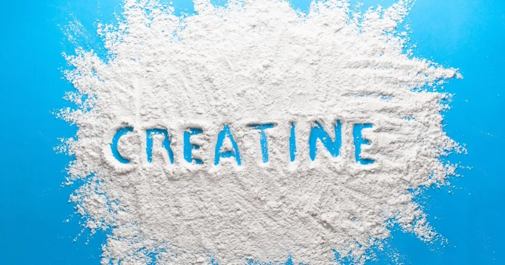 A spread out pile of white Creatine Monohydrate powder against a blue background, with the word "Creatine" traced in it.