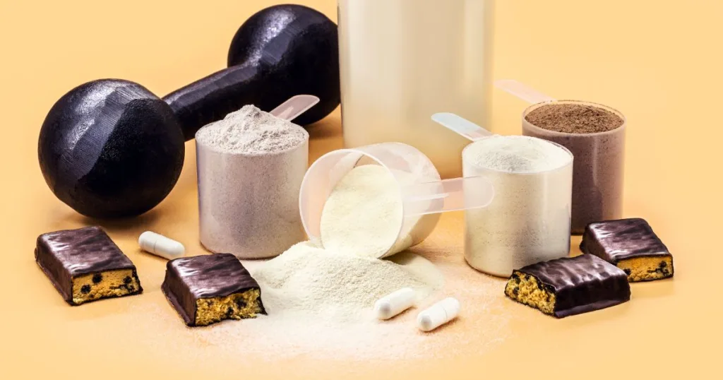 Fitness upplement products with Creatine Monohydrate in several formats including chocolate and vanilla powder in measuring cups, capsules, and chocolate chip nutritional bars alongside a barbell.