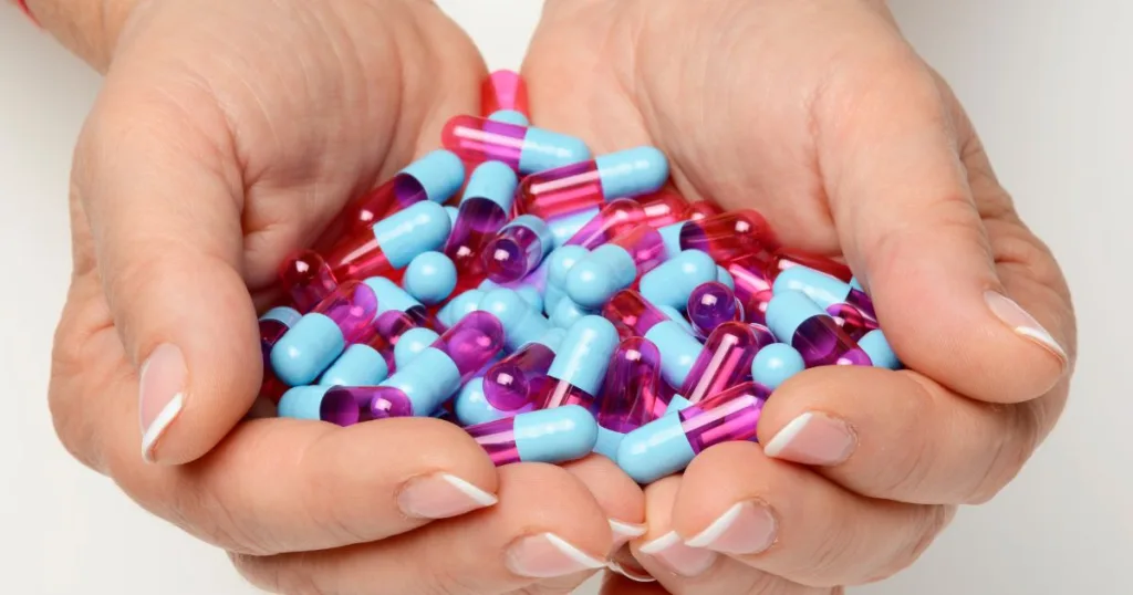 Two cupped hands holding empty two-toned blue and pink capsules.