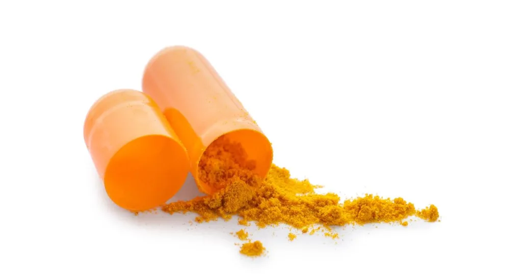 A close-up shot of a separate orange capsule with orange powder material, probably turmeric, spilling out.