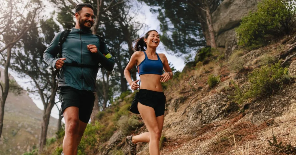 A man and a woman running outside on a hiking trail.