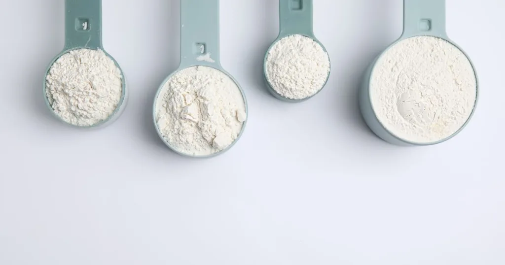 Four measuring cups filled with white amino acids in powder form.