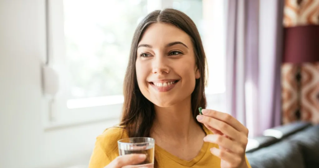 An image of a smiling woman holding a caffeine supplement and a glass of water.
