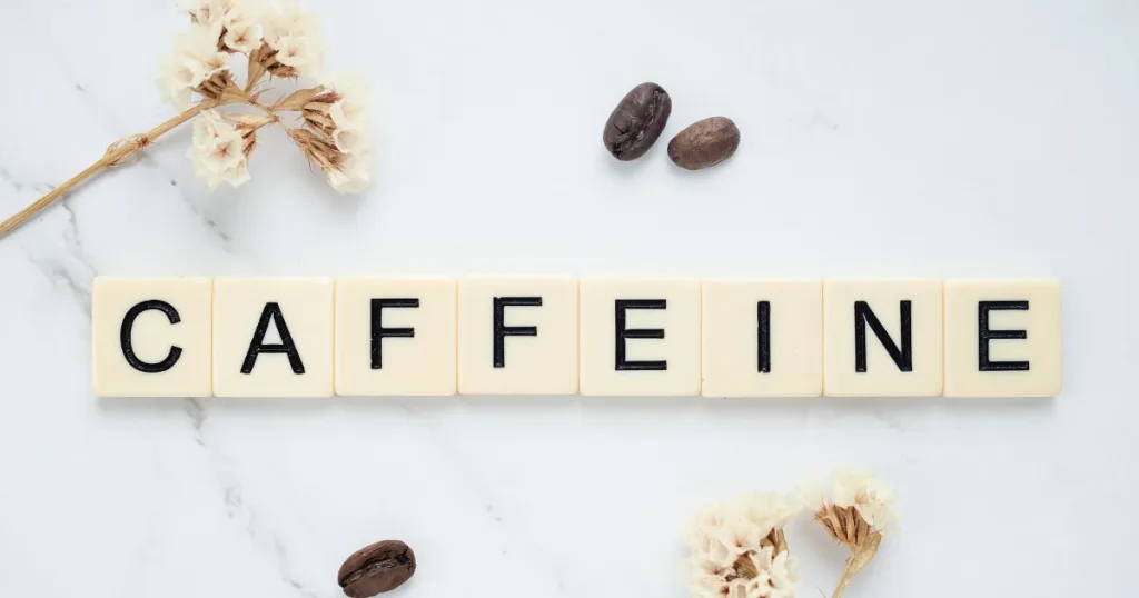 Letter tiles spelling out the word "Caffeine" surrounded by coffee plants and coffee beans.