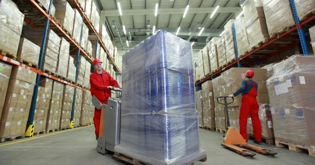 Two workers wearing PPE transporting packaged product in a clean warehouse setting.