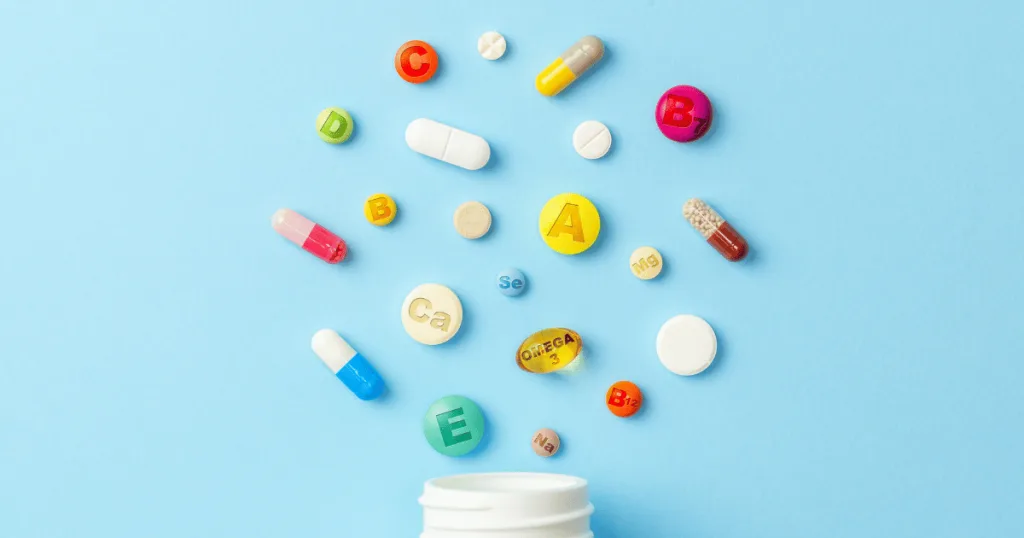 Different types of vitamins spilling out of a supplement bottle against a blue background.
