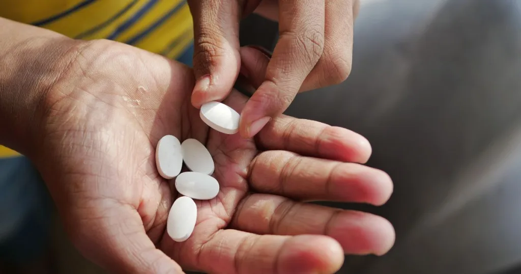 A closeup of a man holding white oblong Magnesium Hydroxide tablets in his palm and picking up one out of it.