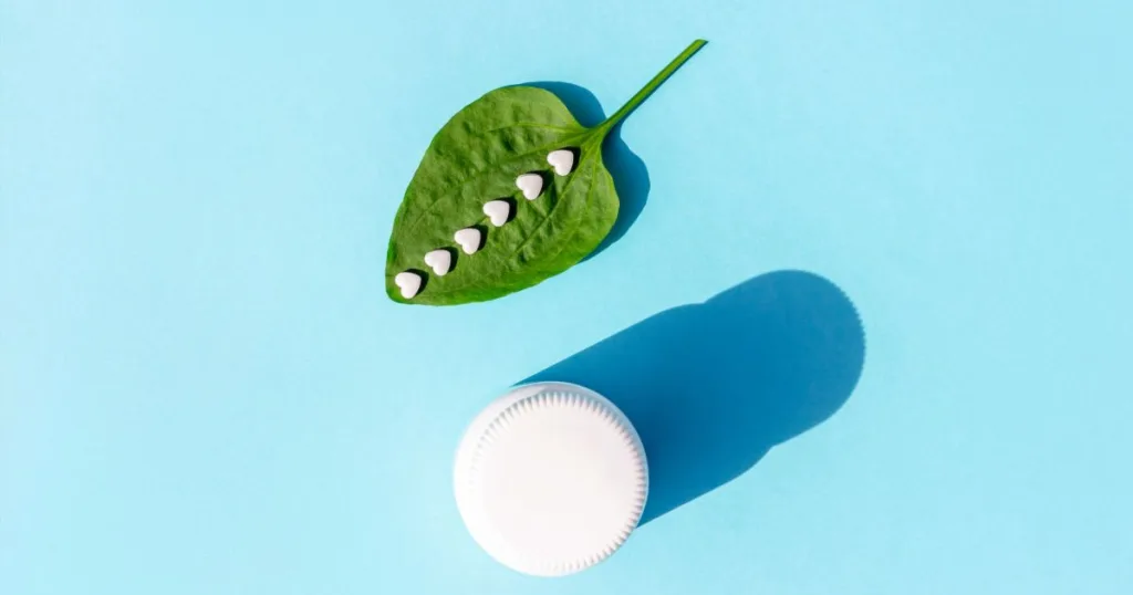 An image of small white, heart-shaped tablets on top of a botanical leaf, next to a supplement bottle against a blue background.