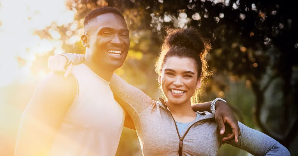 A man and woman in workout clothing with their arms around their shoulders smiling.