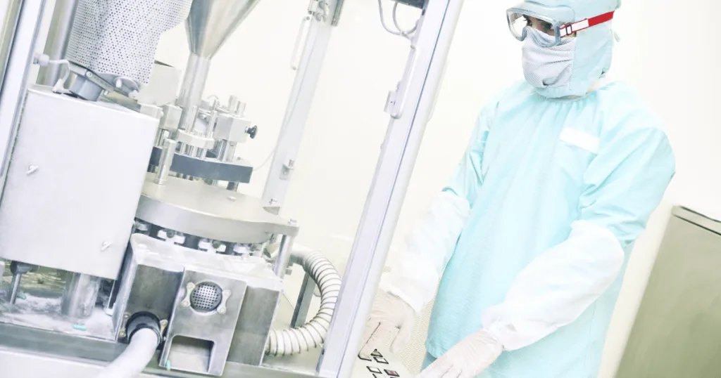 An image of a person, decked out in PPE, operating a high-speed capsule filling machine.