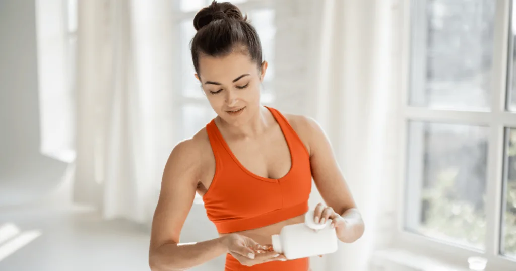 An active woman wearing workout clothes pouring out magnesium supplements from a bottle into her hand.