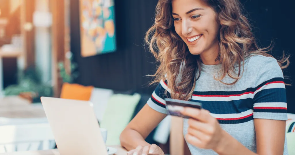 A woman smiling with a credit card in her hand, staring at a laptop screen.