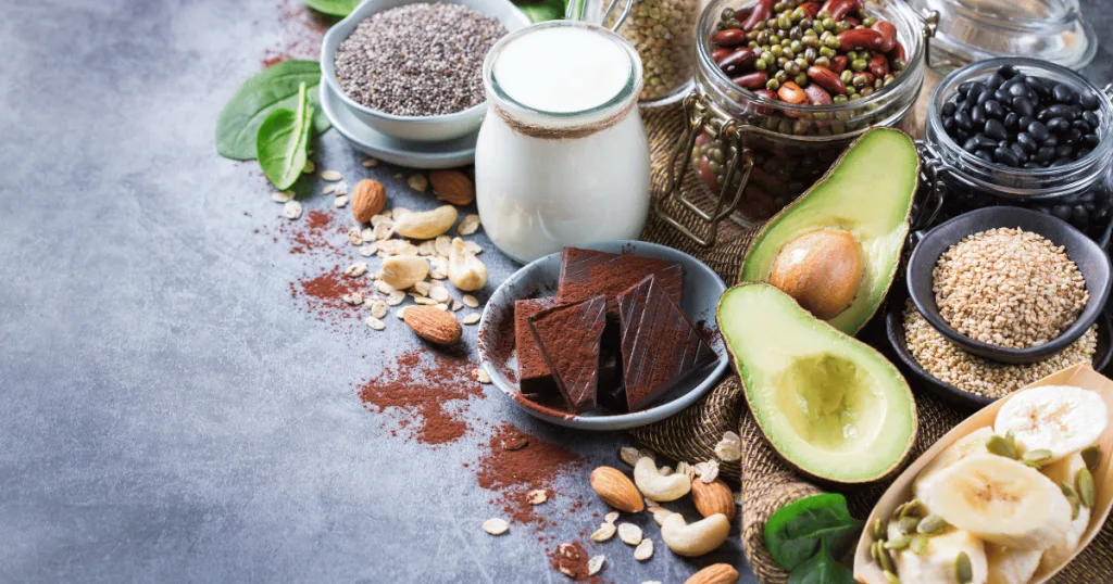 A group of various foods rich in magnesium, such as dark chocolate, avocado, grains, beans, bananas, seeds, and leafy greens.