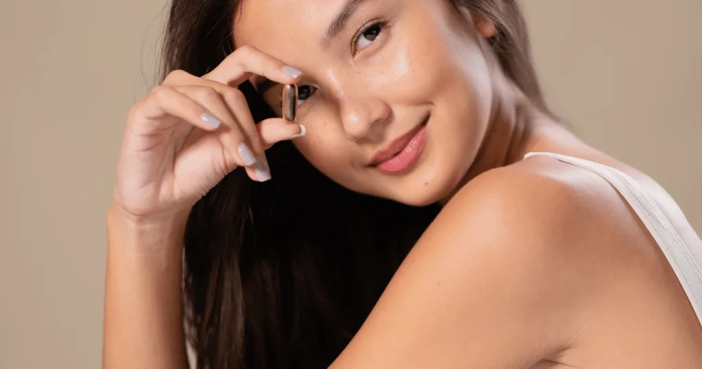 A young woman smiling holding a beauty-from-within gel cap supplement.