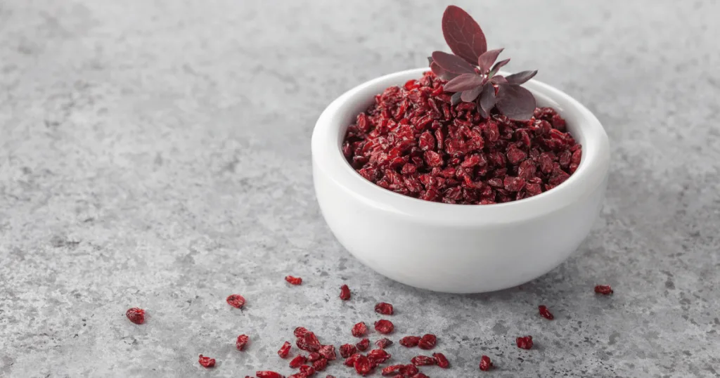 A bowl of dried red barberries, which contain berberine, with fresh red barberry leaves on top.