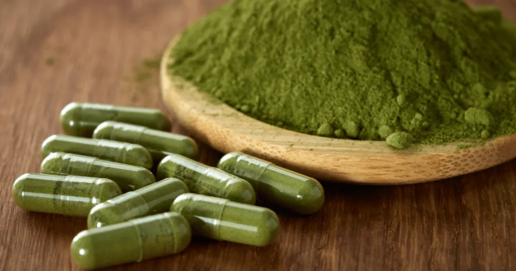 Clear capsules filled with green powdered nutraceutical ingredients, next to a wooden bowl filled with the green nutraceutical ingredient powder.