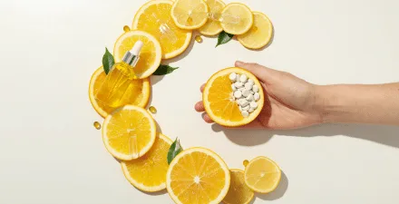 Slices of oranges placed to display the letter C. A hand is also holding a cut orange, with half of it hollowed out and filled with white vitamin c tablets.
