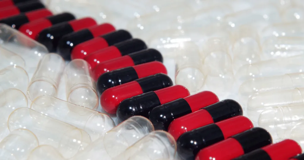 A close up shot of a line of red and black capsules surrounded by clear empty capsules.