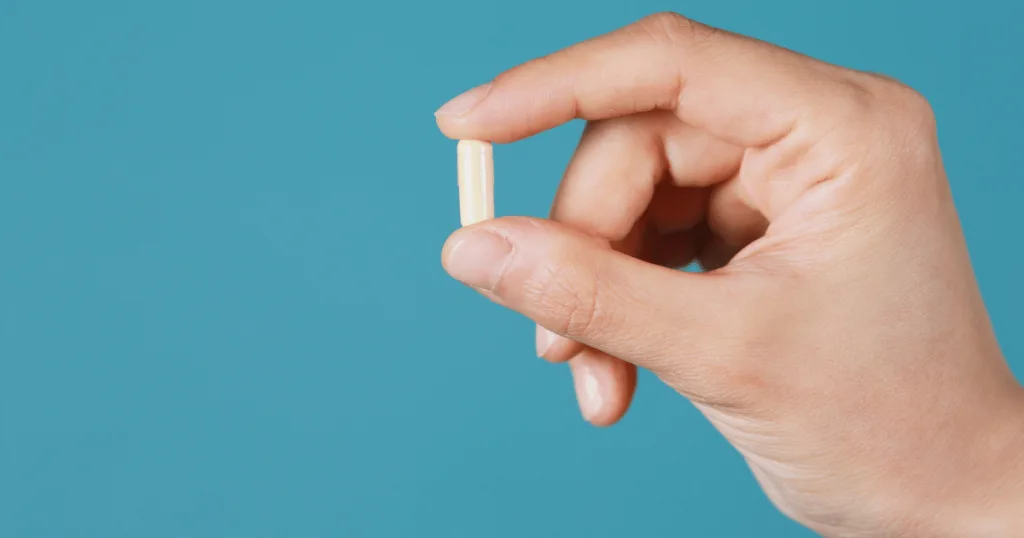 A close up shot of a hand holding a white capsule between the thumb and forefinger. 