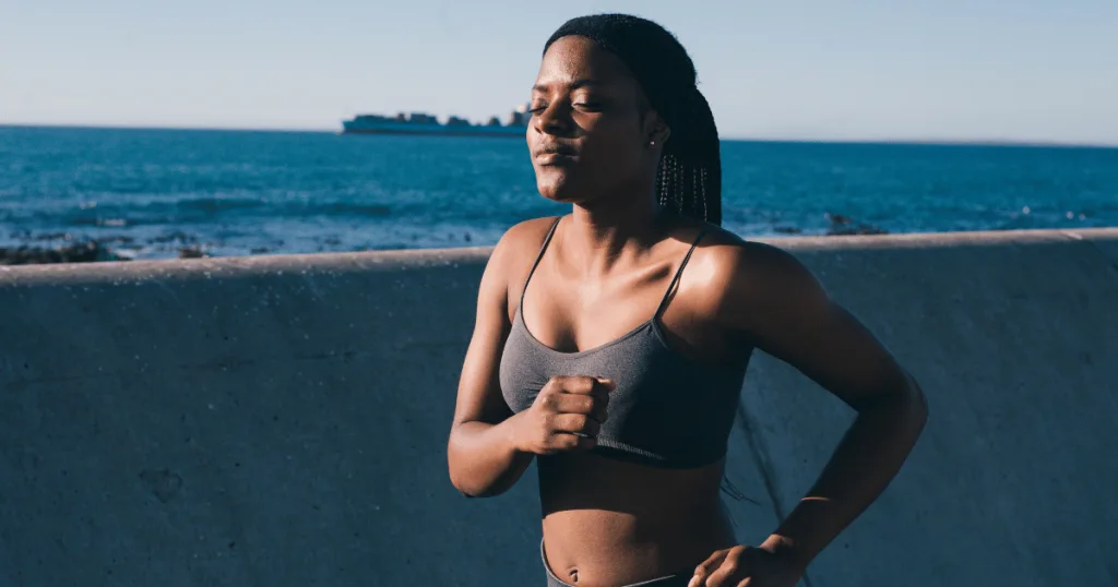 A healthy young woman wearing exercise clothing jogging next to a seawall.