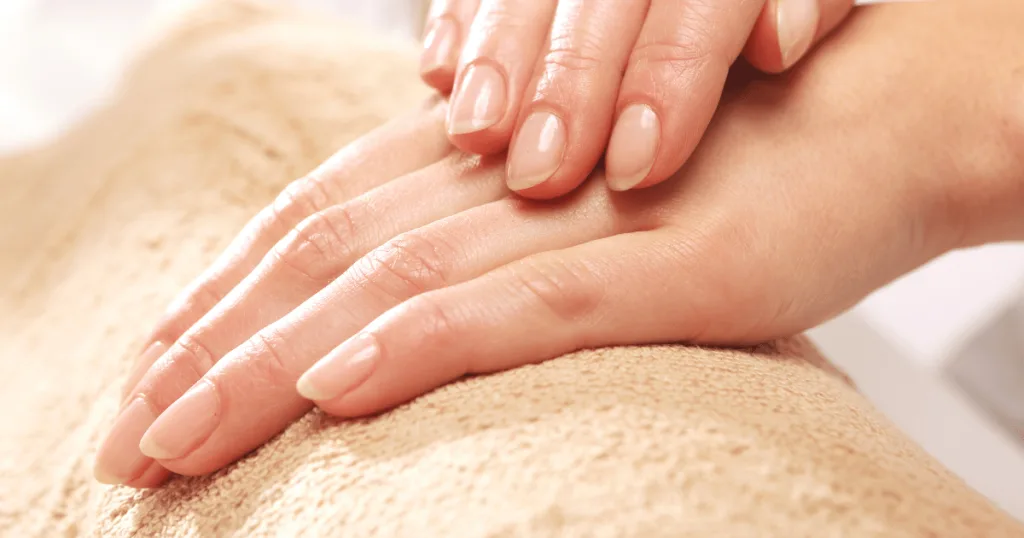 A pair of hands resting on a surface, with glossy, clear nails.