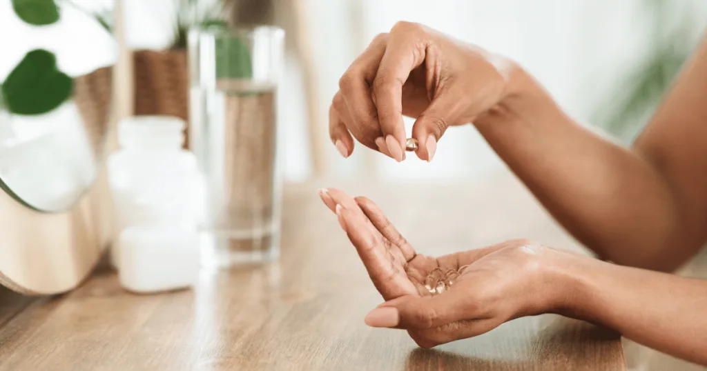 A woman dropping gelcap beauty supplements from one hand into the palm of the other. A glass of water is in the background.