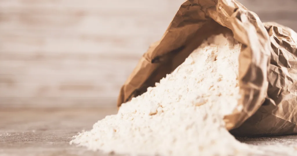 A sack of white powder lying on the ground. Some white powder is spilling out.