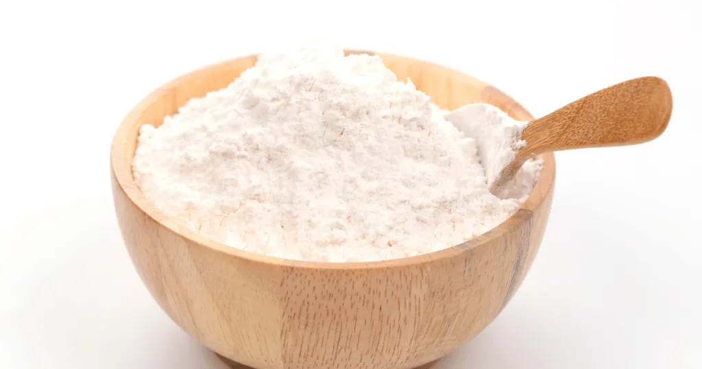 Powdered xanthan gum inside a wooden bowl with a wooden spoon.