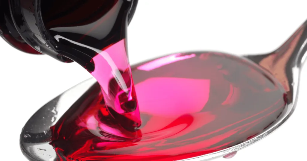 A close up shot of a pink cough syrup being poured into a spoon.