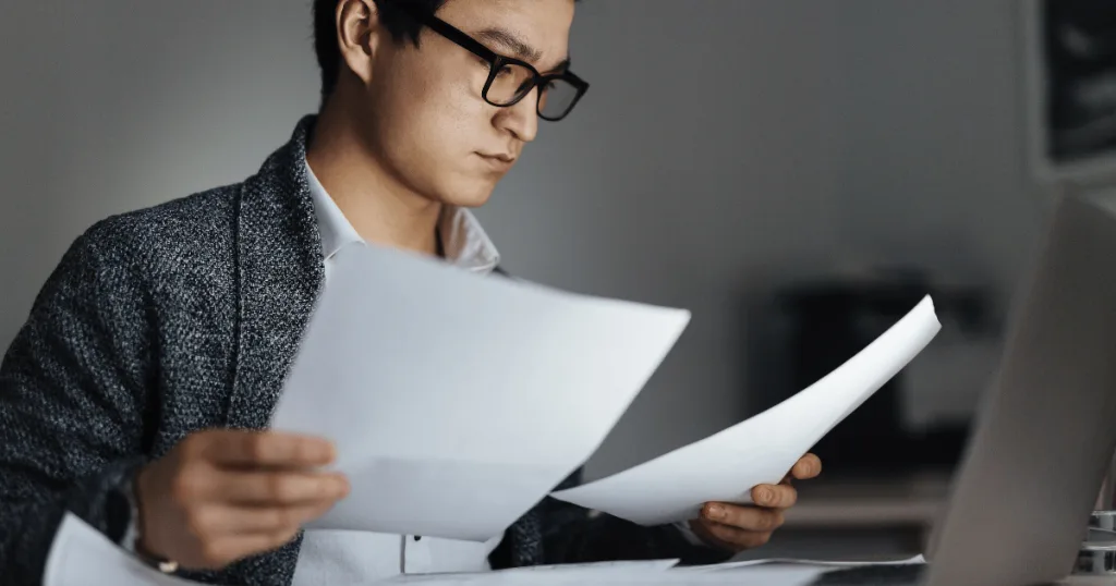 A professional sitting at a desk before a laptop looking at documentation.