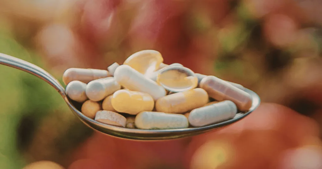 A close up shot of a metal spoon holding different types of supplements, including tablets and capsules.
