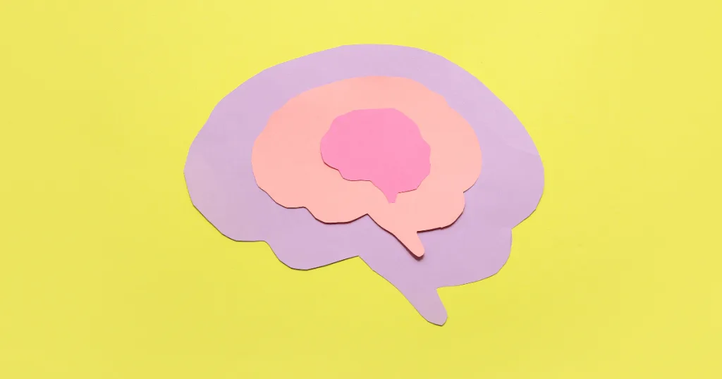 Purple, orange, and pink paper cut outs of a human brain against a yellow background.