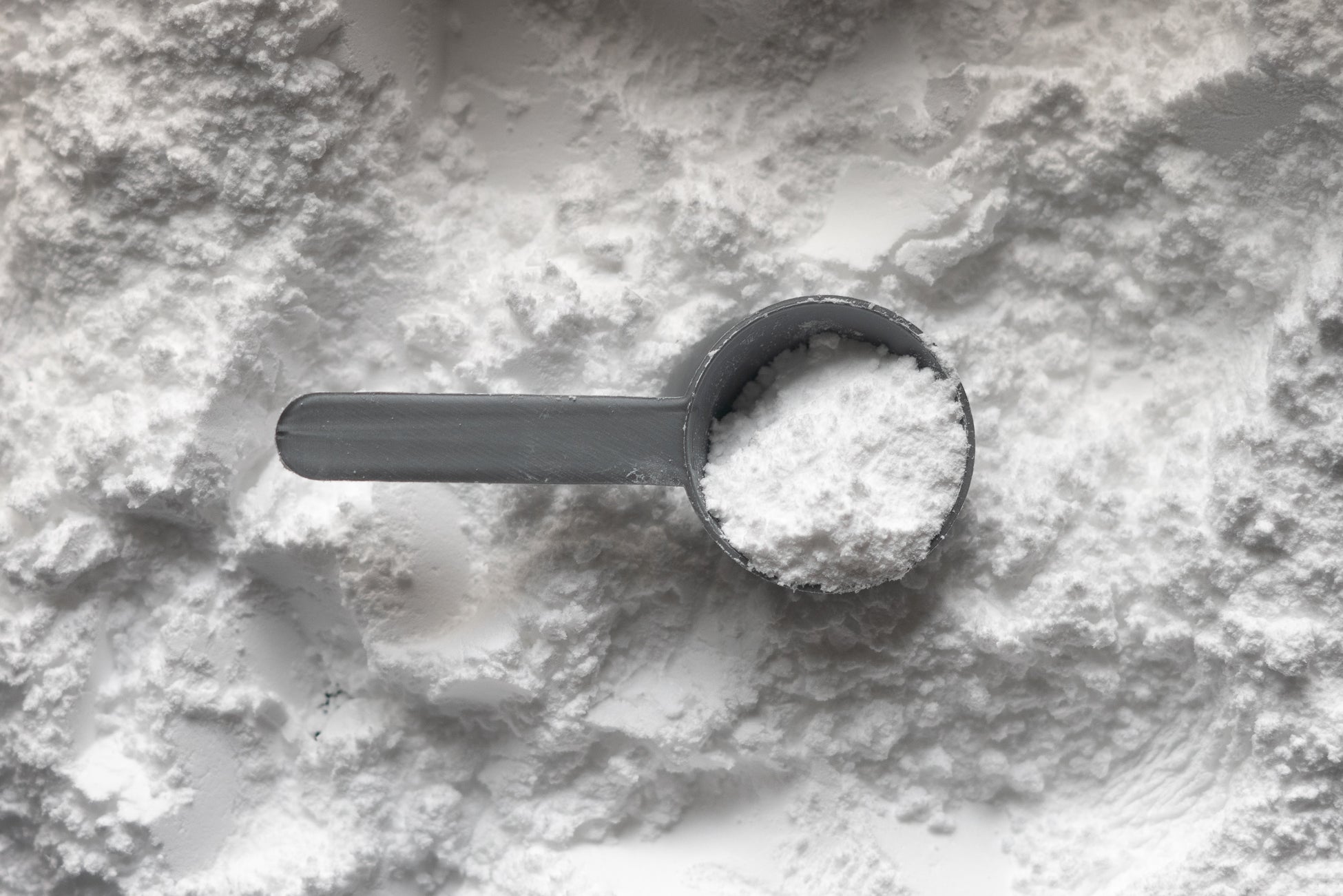 Half-filled ingredient measuring cup resting on a background on white powder.