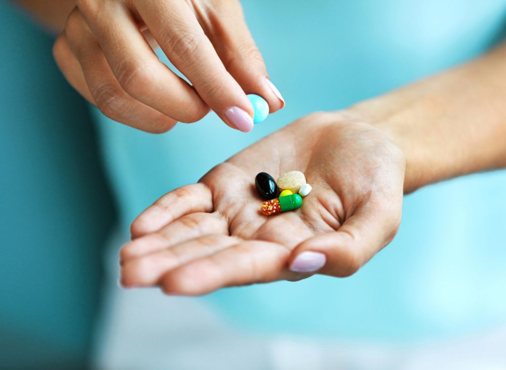 One hand picking up pill among different supplements from the other hand's palm.