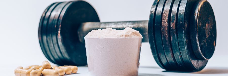 Powder whey protein in a scoop next to filled capsules and barbell