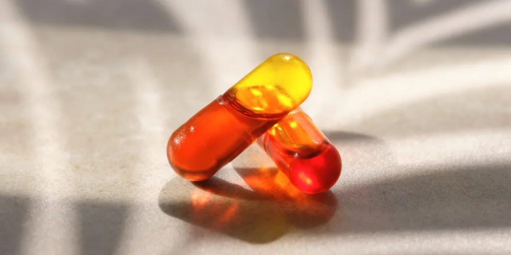 Close up of two piece yellow/clear HPMC capsules with red liquid content.