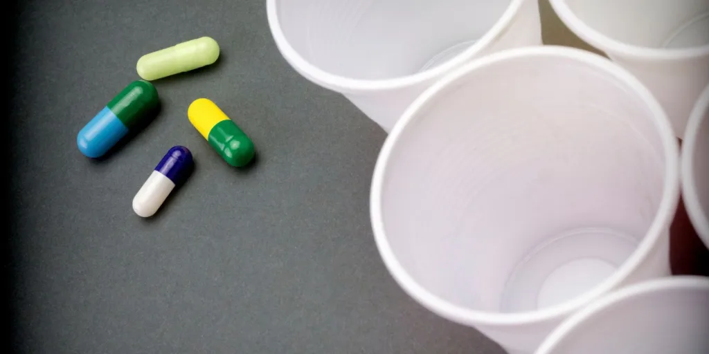 Capsules of varying sizes and colors next to empty plastic cups.